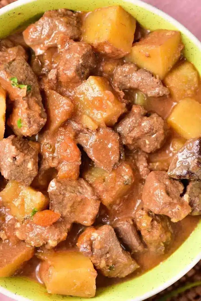 A close-up view of a bowl filled with a hearty beef stew, featuring tender chunks of beef, potato pieces, and a rich brown sauce. The stew appears thick and savory, with visible herbs and vegetables mixed in—reminiscent of a classic Venison Stew Recipe.