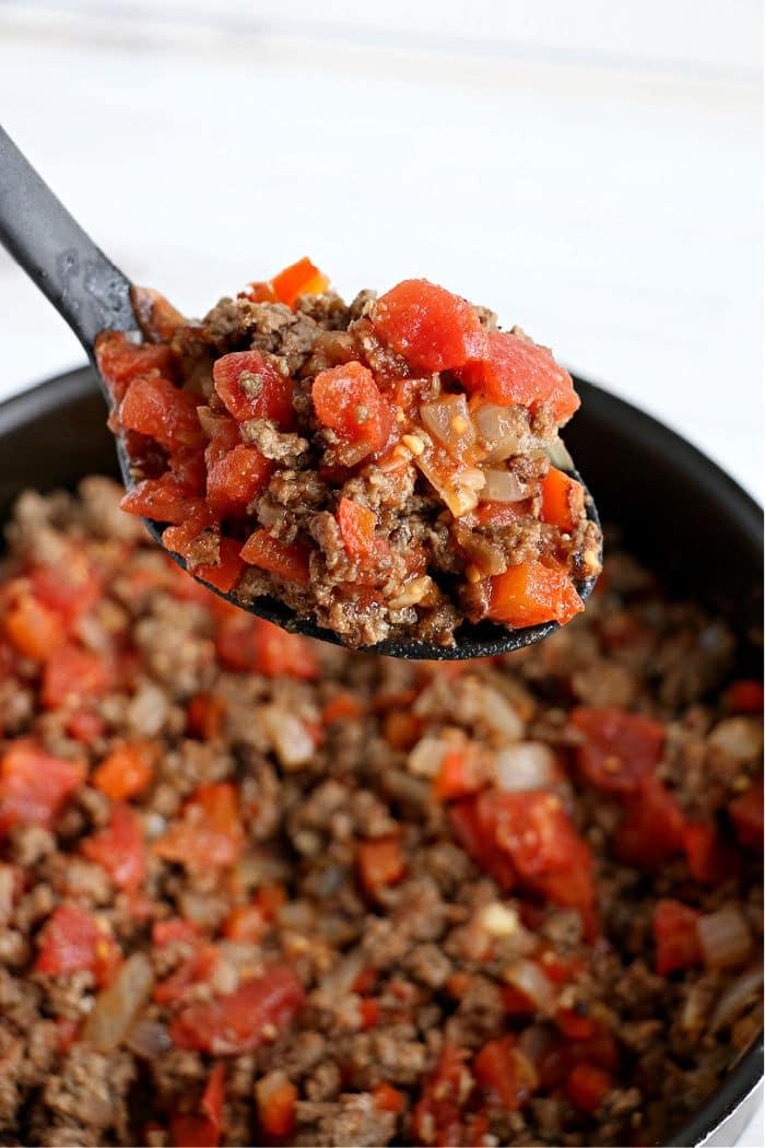 A spoonful of cooked ground beef with diced tomatoes, onions, and peppers held over a pan—an easy idea for what to cook with ground beef tonight.