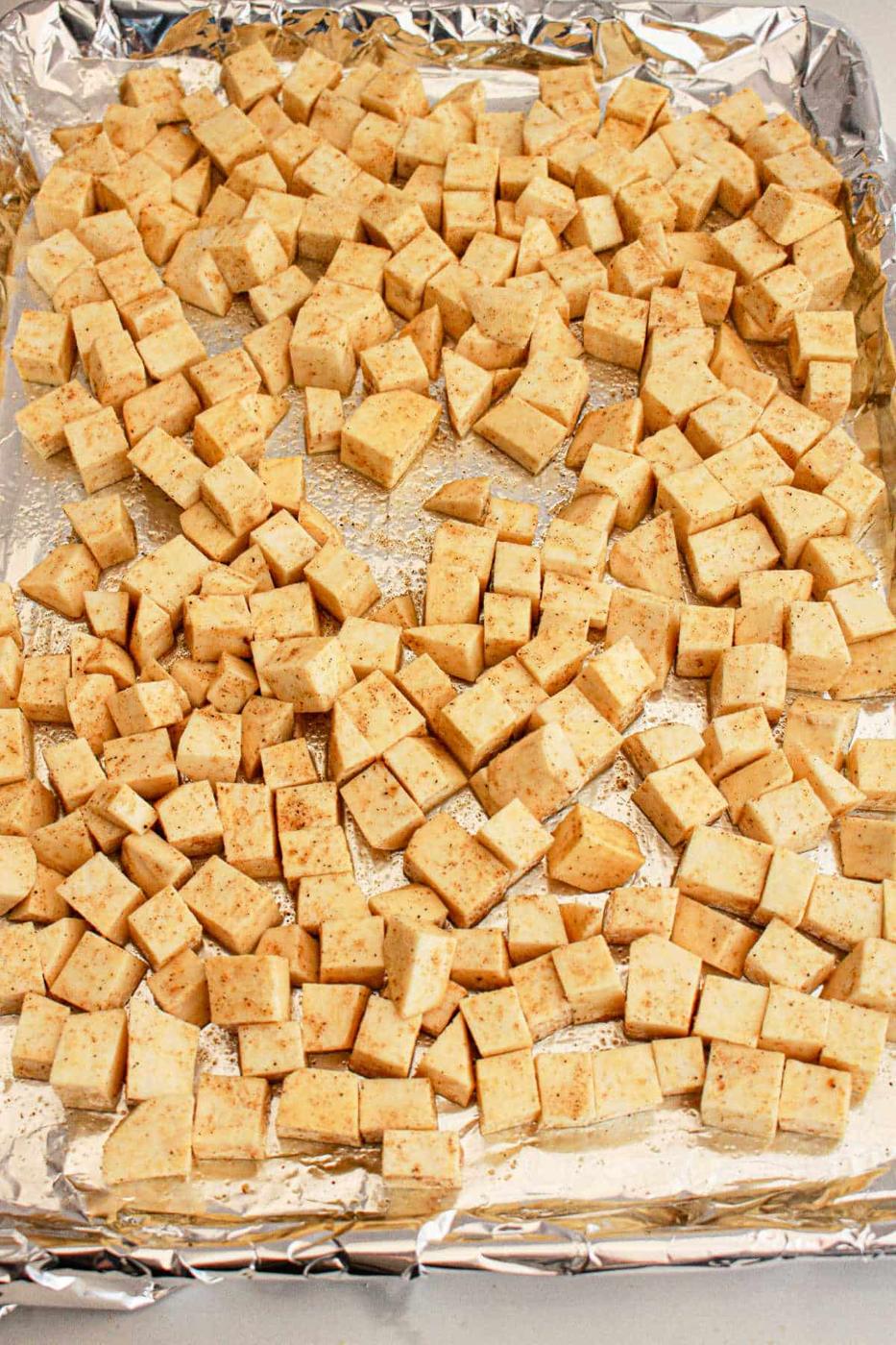 Cubed sweet potato seasoned and spread on a foil-lined baking sheet, ready to be baked—perfect as a protein-packed addition to any White Sweet Potato Recipe.