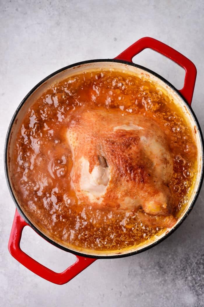 A whole fried chicken simmers in a red pot, enveloped in a rich golden-brown oil.