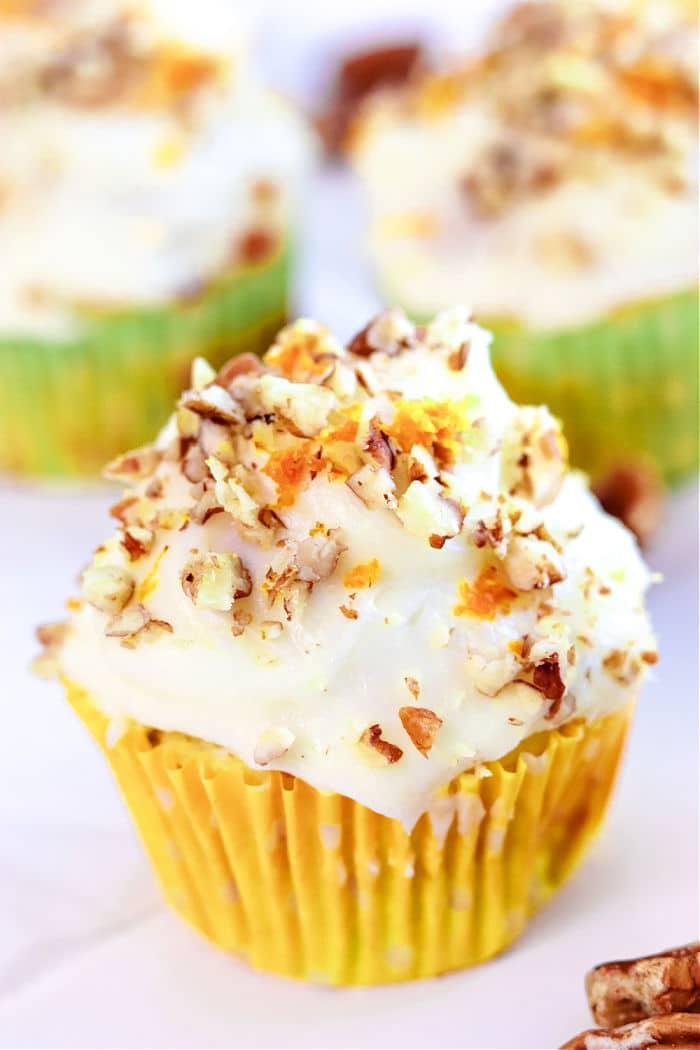 A delightful carrot muffin with cream cheese frosting, sprinkled with chopped nuts, all nestled in a vibrant yellow wrapper. Inspired by the warmth of zucchini carrot muffins, it balances sweetness and texture perfectly.