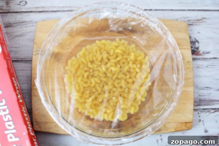 Effortless Microwave Pasta 5 Cooking noodles in the Microwave, showing the bowl covered with plastic wrap.