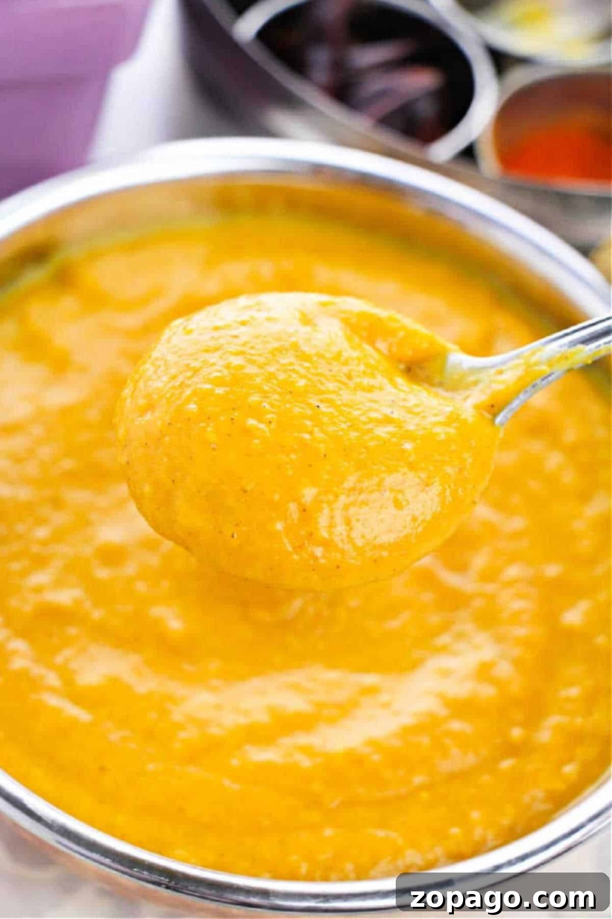 Cozy Canned Pumpkin Soup 2 A spoon holding thick, creamy Pumpkin Soup with Canned Pumpkin hovers over a bowl filled with the same golden curry sauce.