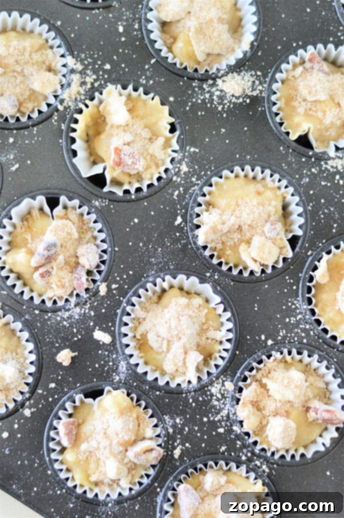 Banana Muffin Minis 4 A muffin tray brimming with batter for mini muffins, crowned with streusel toppings, ready to bake.