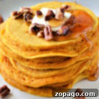 Bisquick Pumpkin Spice Pancakes 6 A stack of pumpkin pancakes with Bisquick is topped with butter, pecans, and a syrup drizzle on a plate.