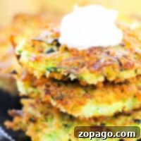 Kabak Mısır Mücveri 8 Three crispy zucchini corn fritters topped with a dollop of sour cream rest elegantly on a dark plate.