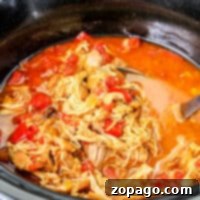 A slow cooker brimming with Mexican shredded chicken, tomatoes, and broth.