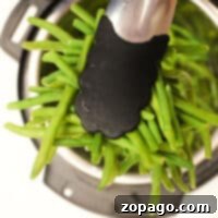 Tongs carefully hold green beans over an Instant Pot, illustrating how to cook frozen green beans effortlessly.