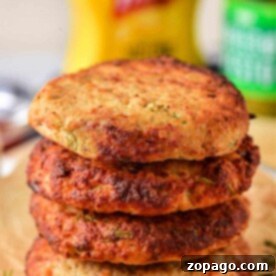 Stack of four golden brown ground turkey patties on parchment paper, with condiments blurred in the background.