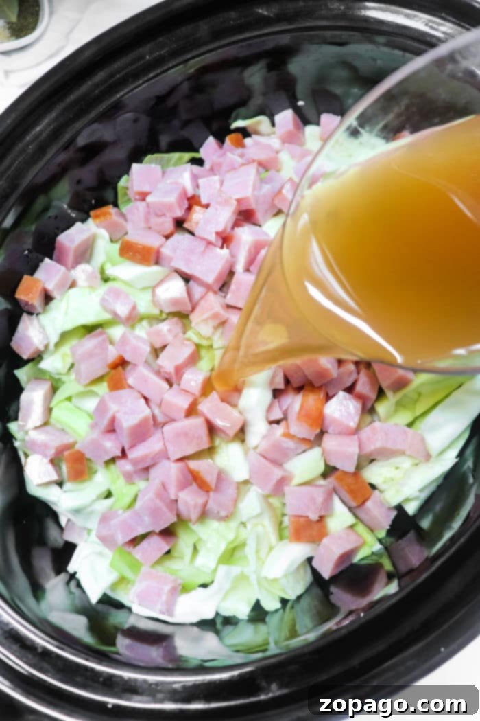 Hearty Cabbage and Ham 4 Simmering a delightful mix of cabbage and ham, with broth poured over the ingredients in a slow cooker for a comforting meal.