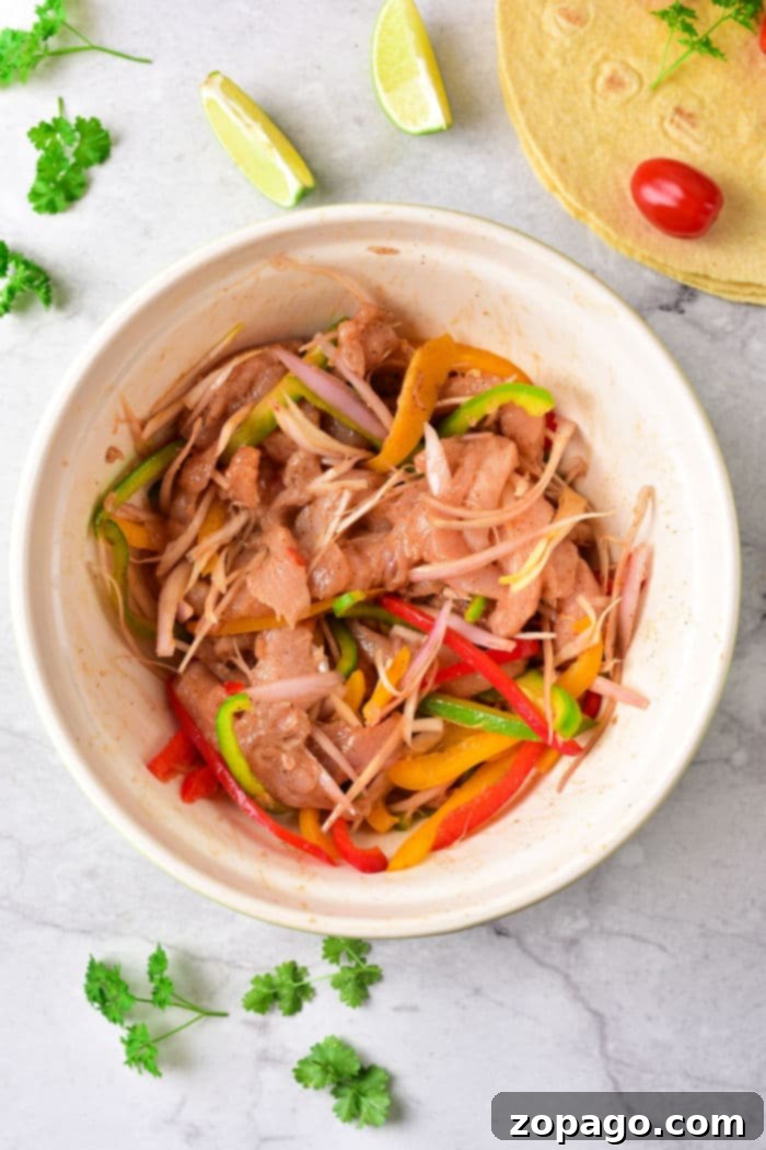 Sizzling Fajita Chicken Tacos 3 A vibrant bowl of marinated chicken, sliced bell peppers, and onions, artfully arranged with fresh lime wedges and parsley, ready for cooking delicious chicken fajita tacos.