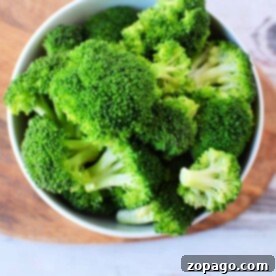 Get Perfect Microwave Broccoli Steamer-Free 7 A bowl brimming with vibrant green broccoli florets sits on a wooden and white surface, ready to be transformed into a quick microwave broccoli masterpiece.