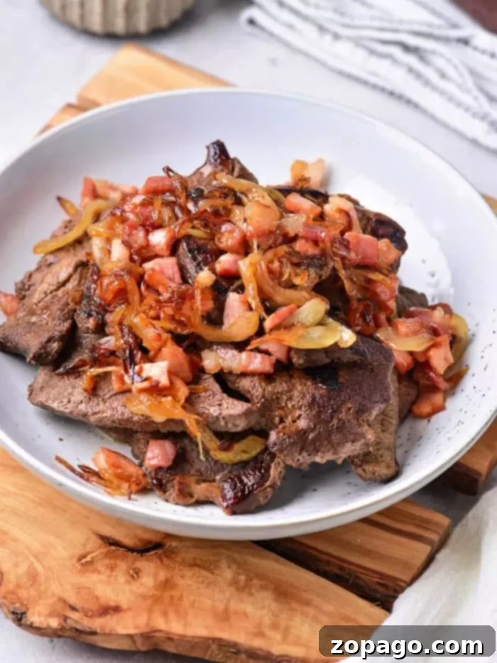 Delicious Pan-Seared Beef Liver 2 A white bowl filled with perfectly cooked beef liver pieces topped with sweet sautéed onions and crispy bacon bits.