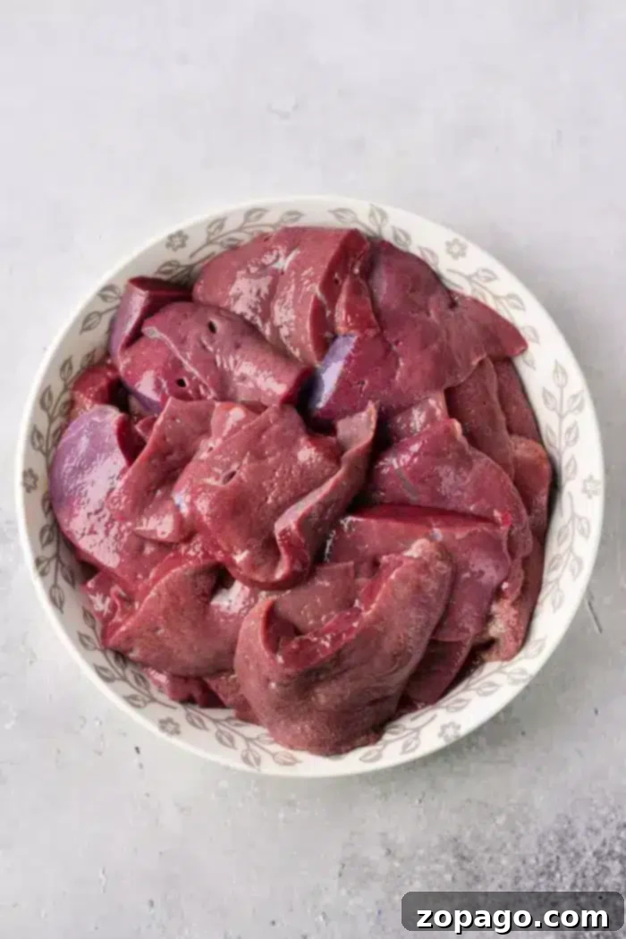 Delicious Pan-Seared Beef Liver 3 A white bowl filled with raw, perfectly sliced calf liver rests on a light gray countertop, ready for the next preparation step.