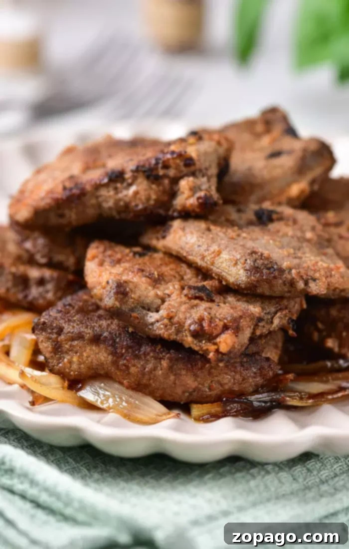 Delicious Pan-Seared Beef Liver 6 A plate of golden-brown fried liver slices stacked elegantly on a bed of sweet caramelized onions, ready for a delicious meal.
