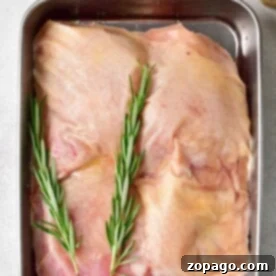 Juicy Baked Frozen Chicken Thighs 5 Raw frozen chicken thighs with rosemary sprigs rest in a tray, ready for baking. Nearby, spices and oil await their turn to enhance the flavor. Perfect for transforming frozen chicken thighs into a delicious meal.