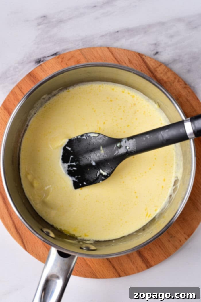 Kickin' Cajun Alfredo 4 A black spatula gracefully stirs creamy rich Cajun Alfredo sauce, all set on a rustic wooden board.