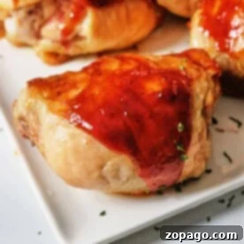 BBQ chicken thighs with a glossy glaze, garnished with herbs, served on a white square plate. Oven-baked to perfection.