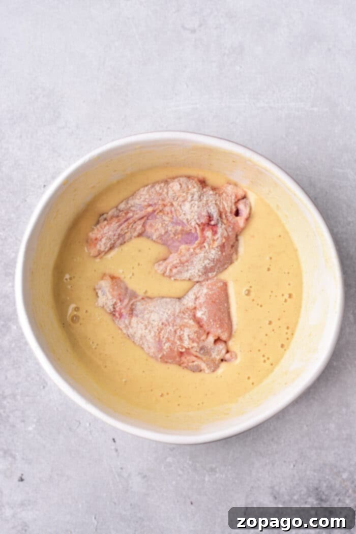 Crispy Deep Fried Chicken Wings Fry Time Guide 4 Raw chicken pieces in a creamy tempura batter sit invitingly in a round white bowl on a gray surface, while you ponder how long to deep fry chicken wings for that perfect crispiness.