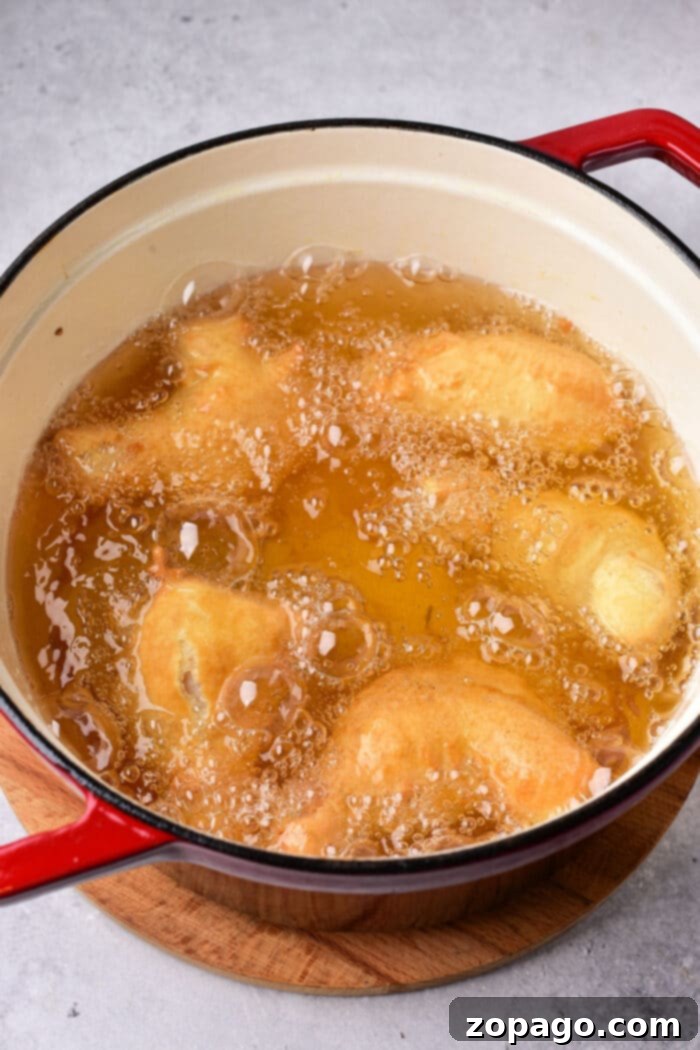 Crispy Deep Fried Chicken Wings Fry Time Guide 5 tempura chicken wings cook in hot oil inside a red pot placed on a wooden surface, much like the ambiance created when timing how long to deep fry chicken wings for that perfect crispy texture.