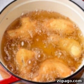 Crispy Deep Fried Chicken Wings Fry Time Guide 6 tempura chicken wings cook in hot oil inside a red pot placed on a wooden surface, much like the ambiance created when timing how long to deep fry chicken wings for that perfect crispy texture.