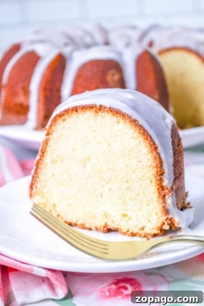 Perfect Homemade Sara Lee Pound Cake 2 A glistening slice of homemade 7Up Pound Cake with lemon glaze, served on a white plate with a gold fork, alongside the beautifully golden bundt cake in the background, ready to be enjoyed.