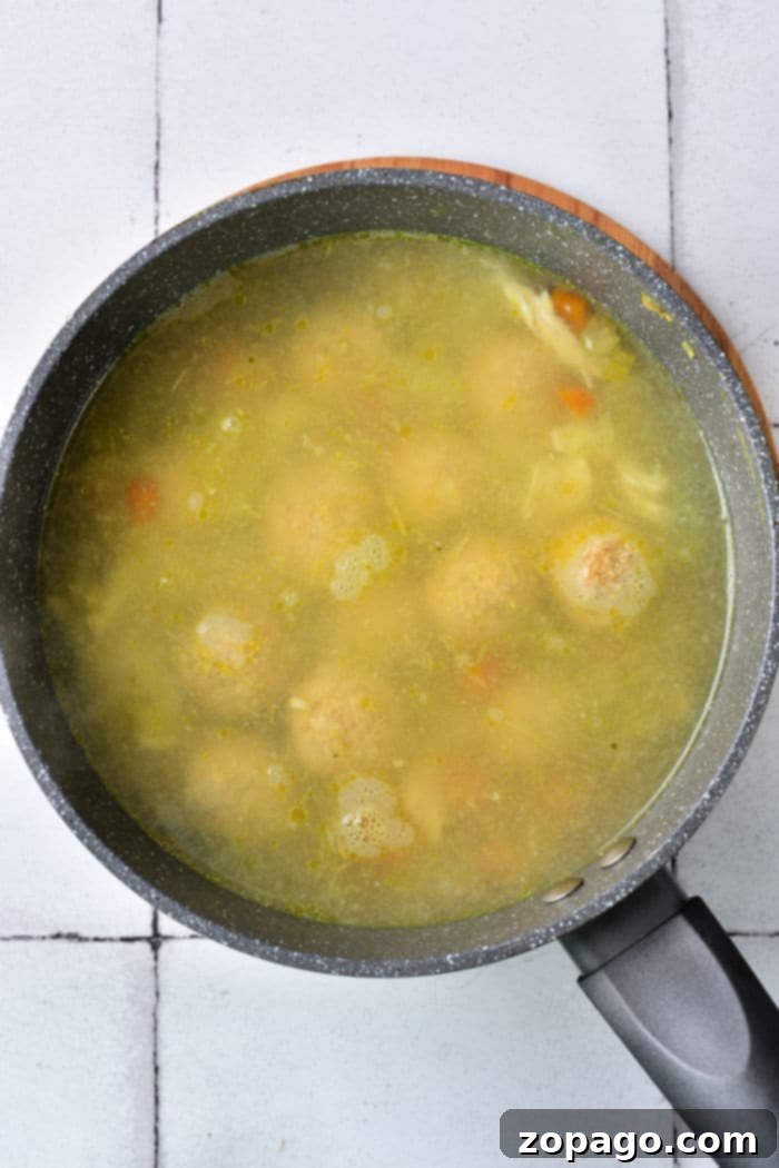 Matzo Ball Explained: Definition and Easy Recipe 6 A close-up of a steaming bowl of matzo ball soup with a rich, golden broth