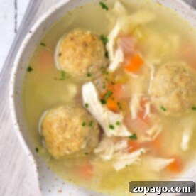 A bowl of rich Chicken Matzo Ball Soup sits invitingly on a wooden surface, brimming with tender chicken and vibrant vegetables.