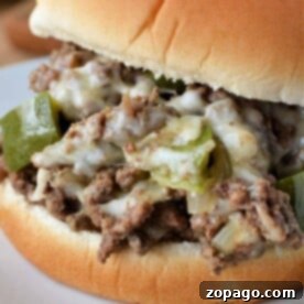 Close-up of a Sloppy Joe sandwich with ground beef, melted cheese, and green peppers on a white plate, evoking the savory essence of a Philly Cheesesteak.