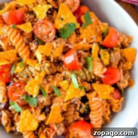 A vibrant one-pot taco pasta salad featuring cherry tomatoes, crushed tortilla chips, and fresh herbs in a white bowl.