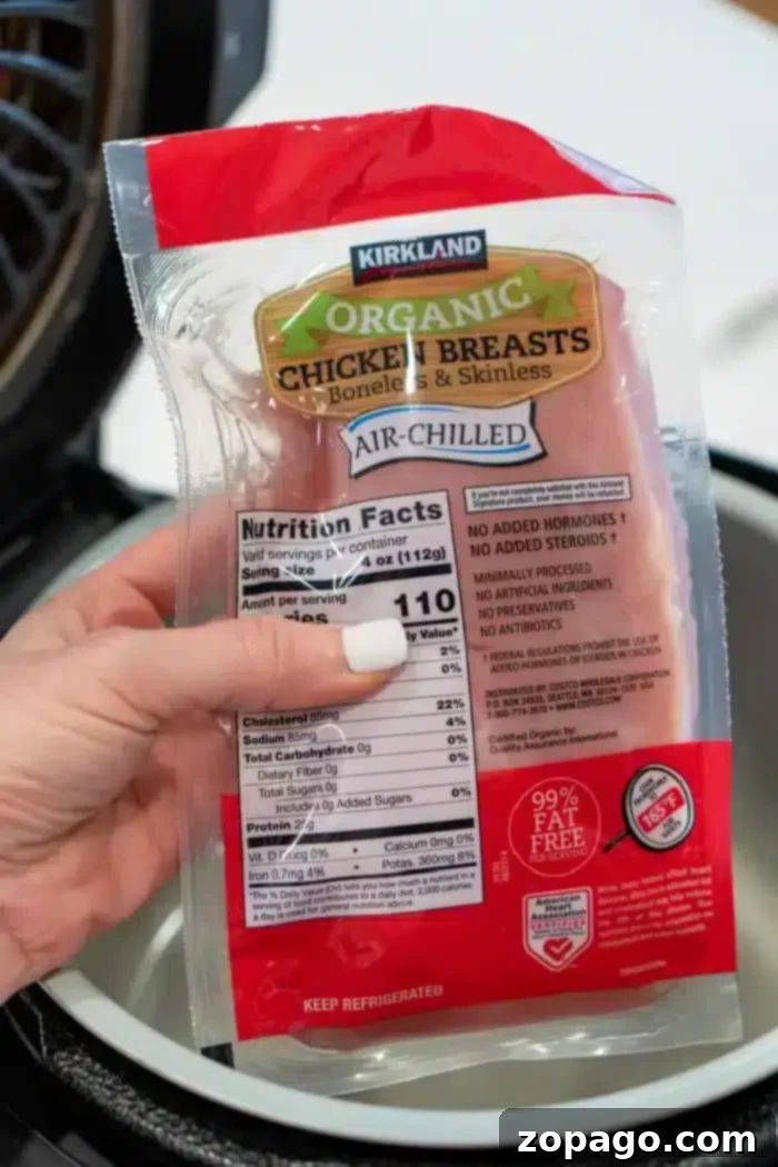 Effortless Ninja Foodi Shredded Chicken 4 A package of Kirkland organic chicken breasts is held by a hand over a Ninja Foodi, ready to transform into delicious shredded chicken. The packaging indicates boneless, skinless, air-chilled.