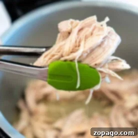 Tongs expertly grasp Ninja Foodi shredded chicken over a simmering pot.