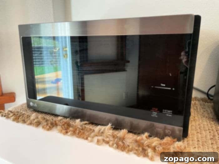 Mastering Rice Cooking Duration 6 A silver LG smart microwave sits on a textured countertop, its control panel ready to help with any task, like how long to cook hot dogs in the microwave. The door is closed, reflecting a window and part of the room on its sleek surface.