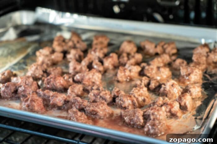 Cooking Ground Beef to Perfection 5 Ground beef sizzle on a foil-lined baking sheet in the oven, turning golden brown. It's crucial to know how long to cook ground beef for perfect doneness and flavor, ensuring a juicy delight every time.
