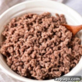 Cooking Ground Beef to Perfection 7 Cooked ground beef in a white bowl with a wooden spoon rests on a cloth napkin, embodying the perfect texture achieved by knowing how long to cook ground meat just right.