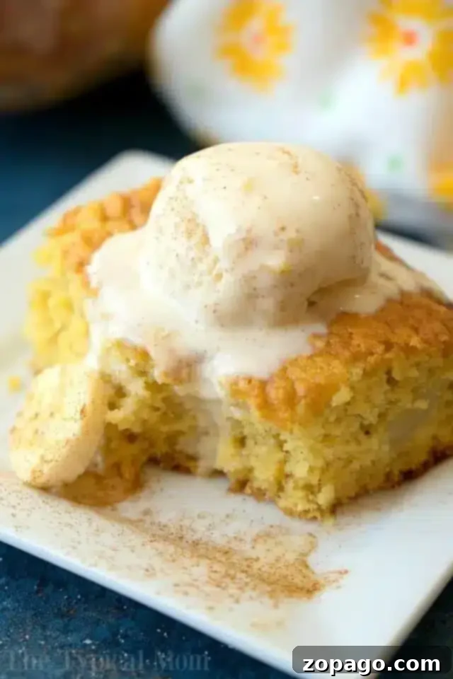 Next-Level Box Cakes Secret Tips for a Homemade Taste 5 A slice of cake, made using clever box cake mix hacks, is topped with a scoop of vanilla ice cream on a white square plate. The cake boasts a light golden color, with a small cookie on the side. Cinnamon graces the top and surrounds the dessert, set against a backdrop of patterned cloth.