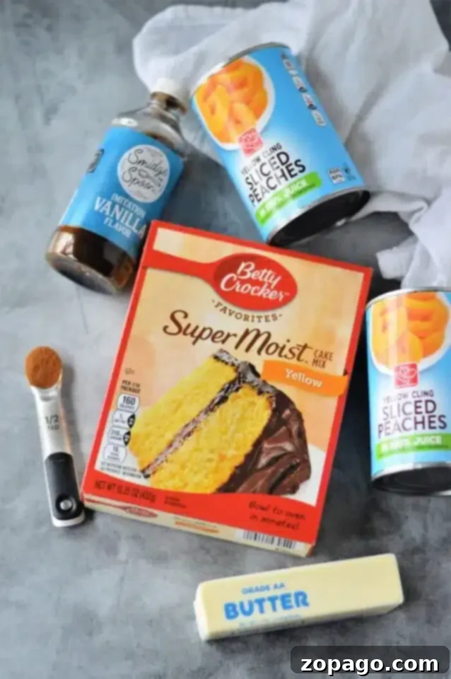 Next-Level Box Cakes Secret Tips for a Homemade Taste 6 A flat lay of baking ingredients on a gray surface features box cake mix hacks like a Betty Crocker Super Moist Yellow Cake Mix, two cans of sliced peaches, vanilla flavoring, a stick of butter, and a 1/2 teaspoon measuring spoon with spice.