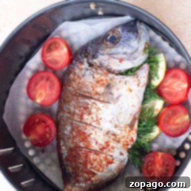 Crispy Air Fryer Whole Fish 5 Air fryer whole fish seasoned with herbs and layered with sliced tomatoes rests in the basket, ready for cooking perfection.