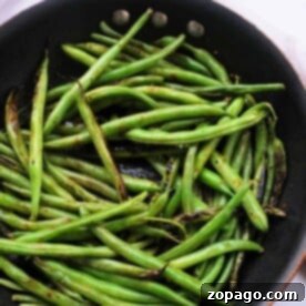 Perfect Stovetop Fresh Green Beans 7 Green beans are sizzling in a black frying pan on a white surface, perfectly capturing the essence of how long to cook fresh green beans on the stove for that ideal flavor and crispness.