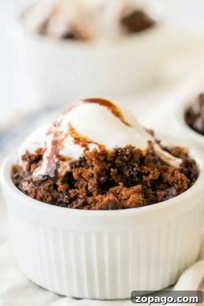Hot Water Cake: Your Secret to Moist Perfection 2 A white ramekin filled with a delectable hot water cake topped with a scoop of vanilla ice cream and drizzled with rich chocolate syrup. Another ramekin with a similar treat is visible in the blurred background.