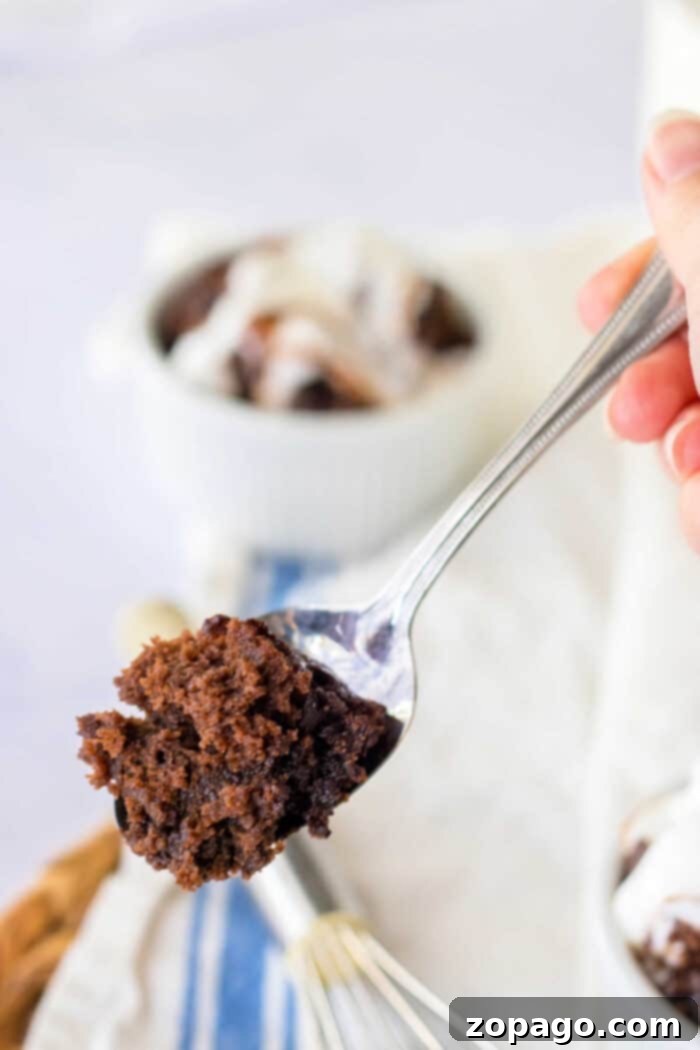 Hot Water Cake: Your Secret to Moist Perfection 6 A spoon cradles a bite of rich hot water chocolate cake, while in the background, a bowl brims with more cake topped generously with whipped cream.