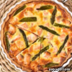 A delicious salmon quiche recipe featuring a savory blend of salmon and asparagus in a white dish, cut into slices. Its elegantly presented on a woven placemat with two forks nearby, ready to delight your taste buds.