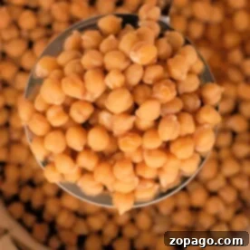 Close-up of a ladle scooping chickpeas from a bowl filled with more garbanzo beans, offering a glimpse into the art of how to cook them.