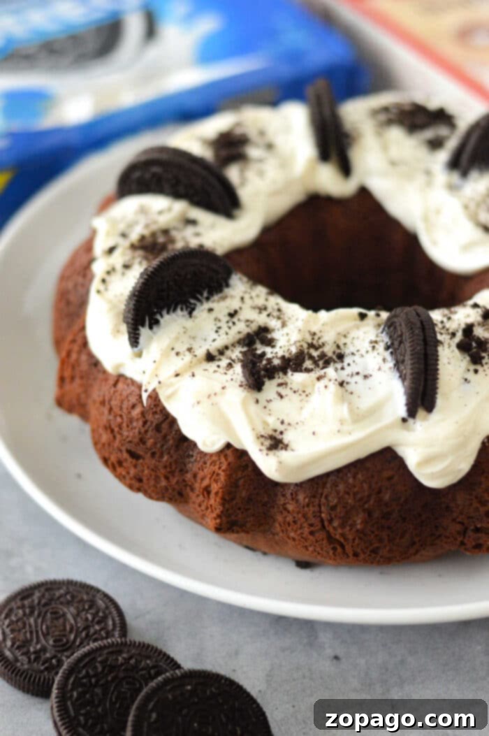 Cookies and Cream Bundt Delight 7 A slice of Oreo Cake with Cake Mix, topped with white frosting and an Oreo cookie, on a white plate.