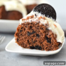 Cookies and Cream Bundt Delight 8 A slice of Oreo Bundt Cake sits elegantly on a white plate, crowned with white frosting and garnished with a classic Oreo cookie.