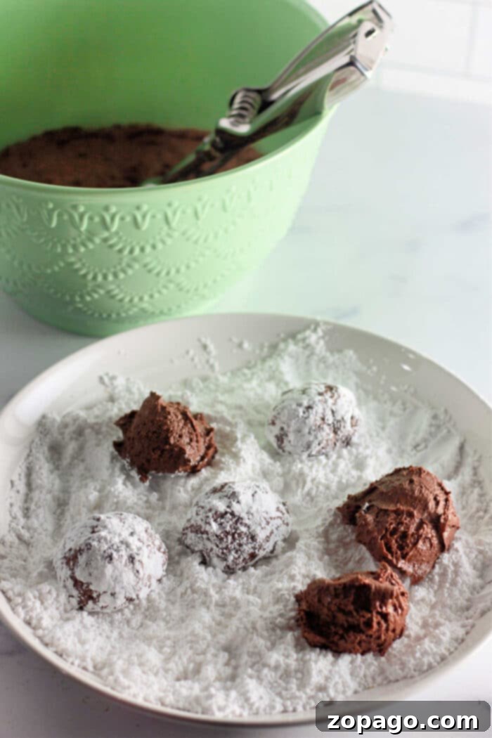 Dreamy Cool Whip Cake Cookies 4 Three Cool Whip cookies, two chocolate and one white, garnished with powdered sugar, sitting on a cooling rack.