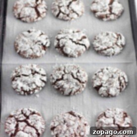 Dreamy Cool Whip Cake Cookies 7 A tray of twelve Cool Whip chocolate crinkle cookies dusted with powdered sugar rests on parchment paper.