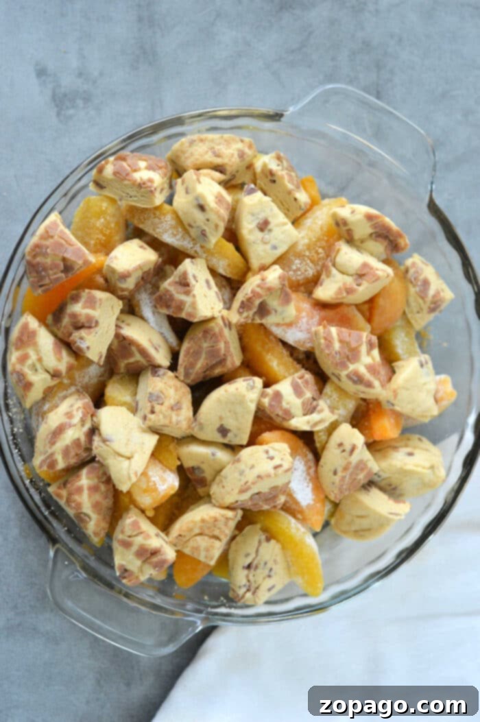 Cinnamon Swirl Peach Cobbler 5 A glass dish brimming with peach slices, chunks of cinnamon rolls, and the warm embrace of cinnamon roll accents create a delightful cobbler experience.