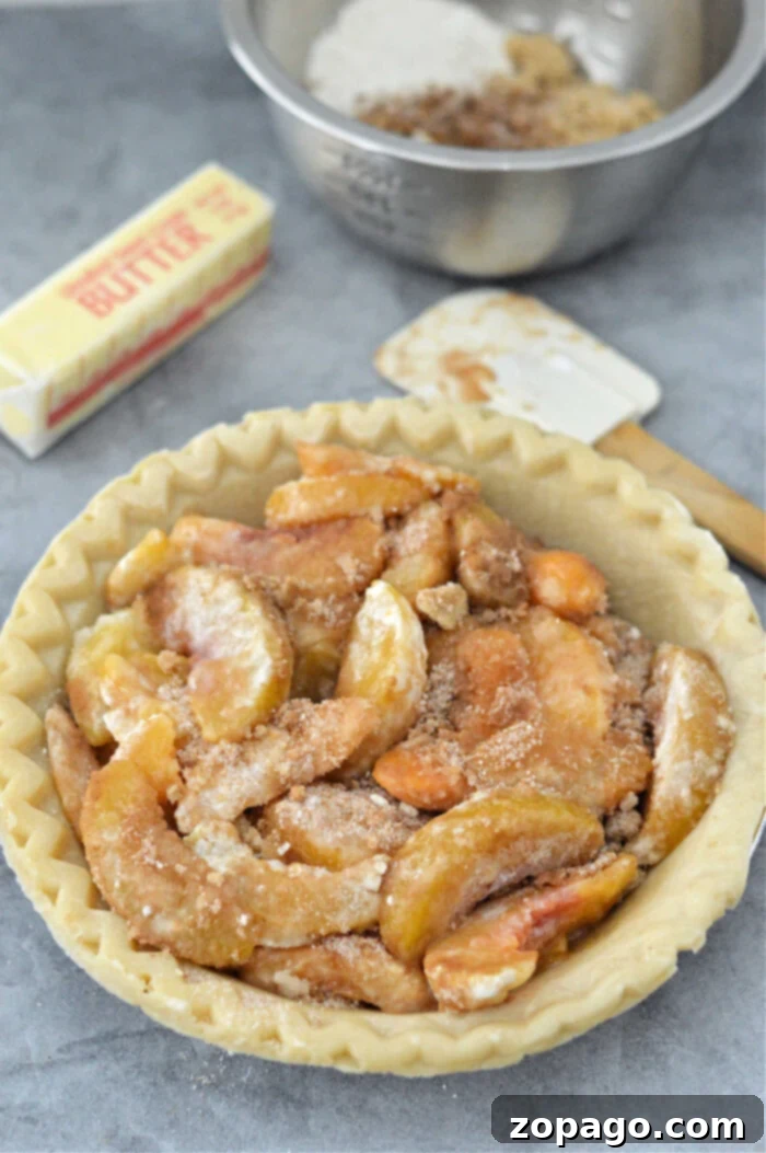Pantry Peach Pie 4 An unbaked peach pie with crumb topping sits invitingly next to a stick of butter, flour, and a metal mixing bowl, reminiscent of preparing a delightful canned peach pie.