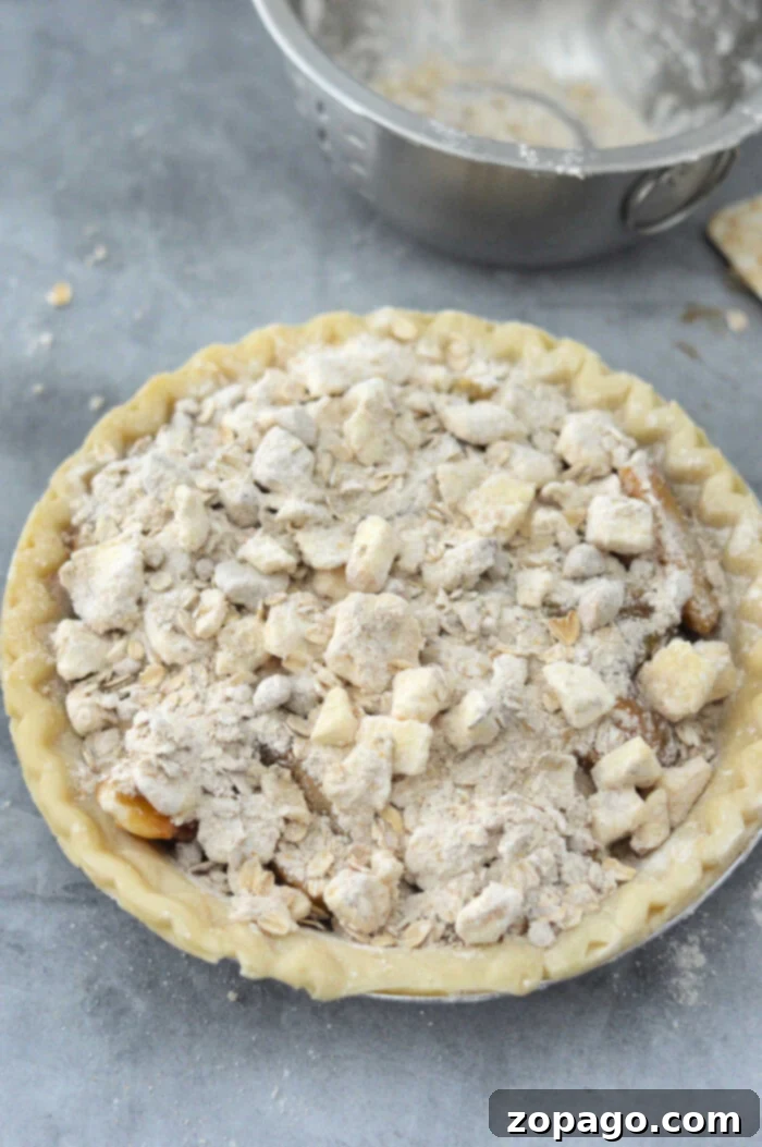 Pantry Peach Pie 6 An unbaked peach pie with crumb topping sits enticingly on a gray countertop, while a metal bowl in the background hints at the possibility of crafting a delightful canned peach pie next.